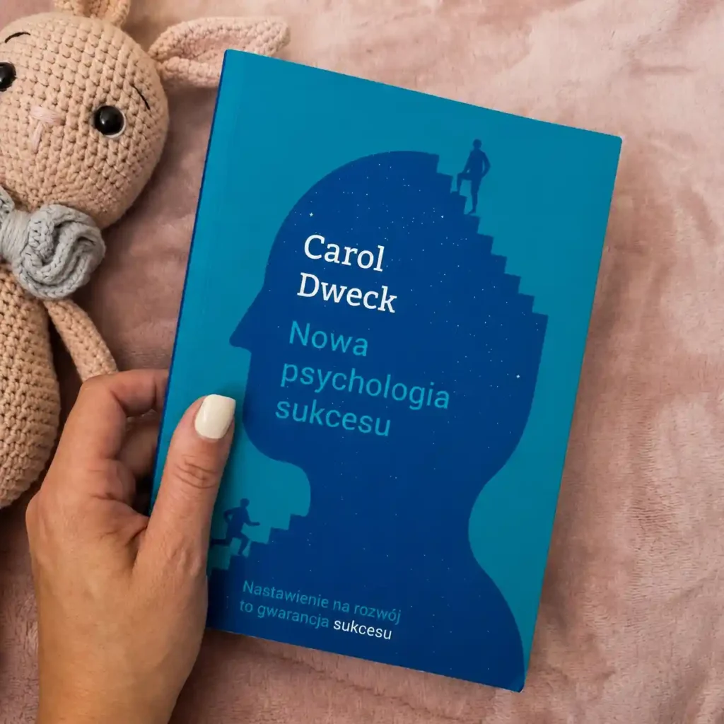 Książka Carol Dweck „Nowa psychologia sukcesu” trzymana w dłoni na różowym kocu